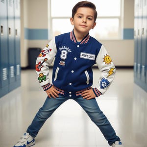 Puede incluir: Una chaqueta universitaria azul y blanca con parches, incluyendo un cohete, una guitarra y un sol. La chaqueta tiene el texto "BIRTHDAY 8" y "JOINED: 2023". Se usa con vaqueros azules y zapatillas blancas.