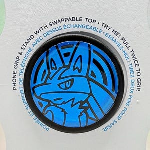Może przedstawiać: Uchwyt i podstawka do telefonu PopSockets z niebiesko-czarnym wzorem. Białe opakowanie zawiera logo PopSockets i informacje o produkcie. Produkt przeznaczony jest do chwytania i stania.