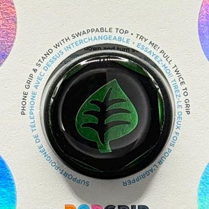 Może przedstawiać: PopSockets PopGrip na białej karcie z iryzującymi krawędziami. PopGrip jest czarny z zielonym wzorem liścia. Karta zawiera logo PopSockets i PopGrip oraz tekst "Phone Grip & Stand with Swappable Top".