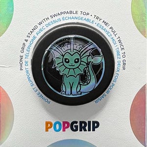 May include: A black PopGrip phone stand with a blue and green graphic of a mythical creature with fins and a tail. The text "TRY ME! PULL TWICE TO GRIP" is printed on the white background.