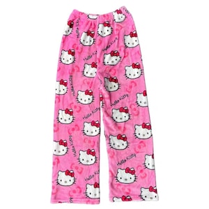 Puede incluir: Pantalones de pijama rosas con un estampado repetido de caras de Hello Kitty con lazos rojos. Las palabras "Hello Kitty" est&aacute;n impresas en los pantalones. Los pantalones est&aacute;n hechos de un material suave y difuso.