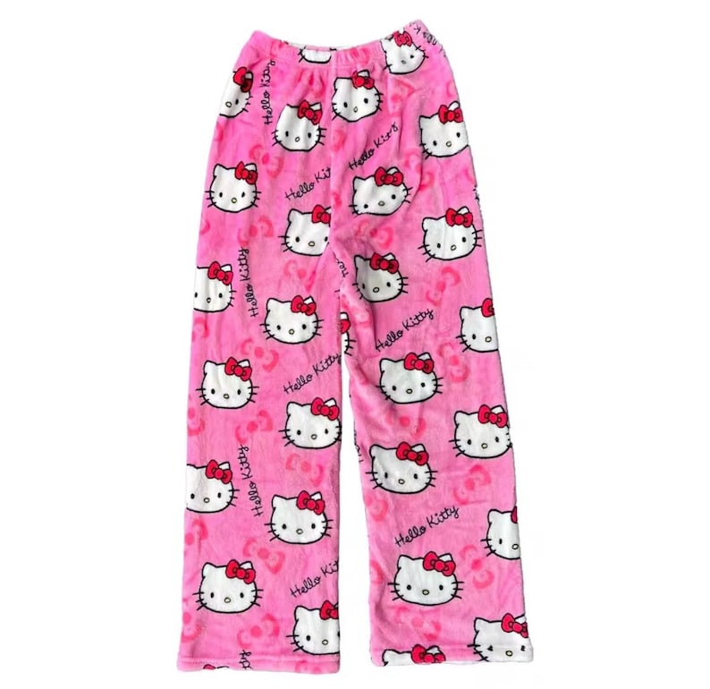 Puede incluir: Pantalones de pijama rosas con un estampado repetido de caras de Hello Kitty con lazos rojos. Las palabras "Hello Kitty" est&aacute;n impresas en los pantalones. Los pantalones est&aacute;n hechos de un material suave y difuso.