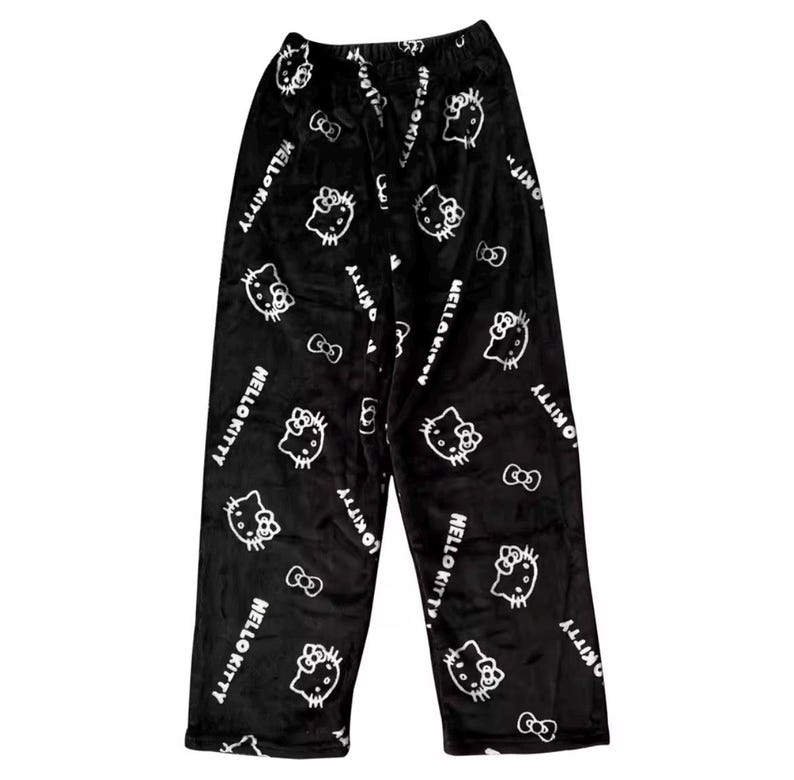 Puede incluir: Pantalones de pijama negros con un patr&oacute;n repetido de caras de Hello Kitty blancas, lazos y las palabras "Hello Kitty". Los pantalones est&aacute;n hechos de un material suave y afelpado.