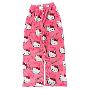 Puede incluir: Pantalones de pijama rosas con un estampado repetido de caras de Hello Kitty con lazos rojos. Los pantalones tambi&eacute;n tienen la inscripci&oacute;n "Hello Kitty". Los pantalones de pijama est&aacute;n hechos de un material suave y afelpado.