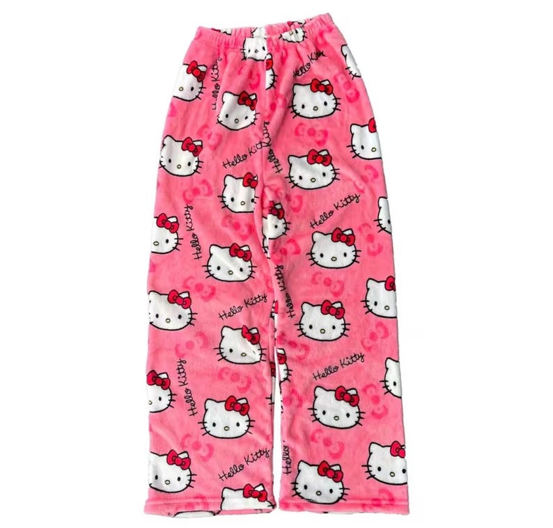 Puede incluir: Pantalones de pijama rosas con un estampado repetido de caras de Hello Kitty con lazos rojos. Los pantalones tambi&eacute;n tienen la inscripci&oacute;n "Hello Kitty". Los pantalones de pijama est&aacute;n hechos de un material suave y afelpado.