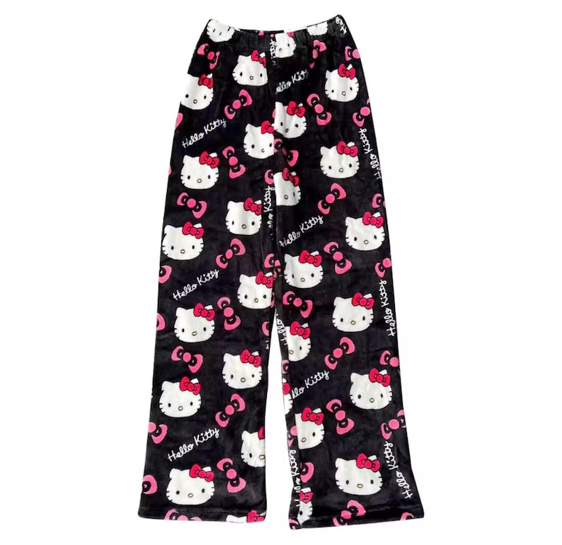 Puede incluir: Pantalones de pijama negros con un patr&oacute;n repetido de caras de Hello Kitty, lazos rosas y las palabras "Hello Kitty" en blanco. Los pantalones est&aacute;n hechos de un material suave y afelpado.