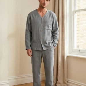Op de afbeelding: Een grijze linnen pyjamaset. De top met lange mouwen heeft een V-hals, een knoopsluiting en een borstzak. De broek heeft rechte pijpen. De outfit is gemaakt van een zachte, lichte stof, perfect om te loungen of te slapen.