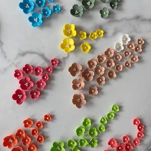 Pode incluir: Conjunto de 10 flores de açúcar de diferentes cores com centros de pérolas. As flores estão dispostas em grupos de diferentes tamanhos e cores.