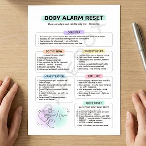 May include: A white printed sheet titled "BODY ALARM RESET" with instructions for calming the body. The sheet includes sections on core ideas, a 2-minute body reset, and quick reset techniques. A silver pen rests on a wooden surface.