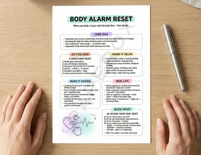 May include: A white printed sheet titled "BODY ALARM RESET" with instructions for calming the body. The sheet includes sections on core ideas, a 2-minute body reset, and quick reset techniques. A silver pen rests on a wooden surface.
