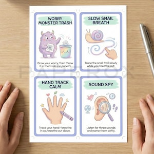 May include: Four illustrated cards with calming techniques: "Worry Monster Trash," "Slow Snail Breath," "Hand Trace Calm," and "Sound Spy." Each card features a colorful illustration and instructions. A silver pen rests on the wooden surface.