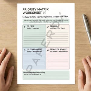 May include: A white Priority Matrix Worksheet with black text, including the title and instructions. The worksheet is divided into four sections with headings such as "Do First" and "Schedule." A silver pen lies on the wooden surface beside the worksheet.