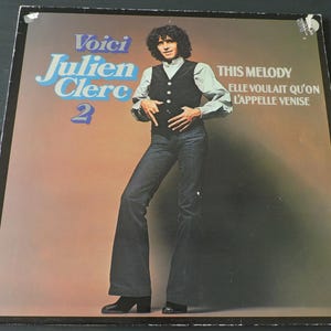Könnte beinhalten: Vintage Vinyl-Schallplattenhülle mit Julien Clerc. Das Albumcover trägt den Text "Voici Julien Clerc 2" in Blau und Weiß. Das Albumcover trägt auch den Text "THIS MELODY" und "ELLE VOULAIT QU'ON L'APPELLE VENISE". Das Albumcover zeigt ein Foto von Julien Clerc.