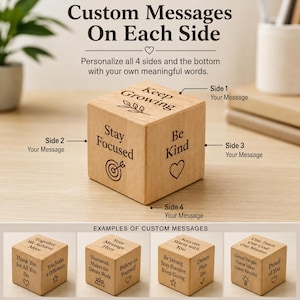 May include: A light-colored wooden cube featuring laser-engraved text and icons on its sides. The top displays 'Keep Growing' with a leaf icon, while the sides show 'Stay Focused' with a target icon and 'Be Kind' with a heart icon.