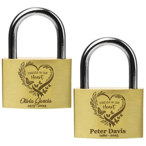 May include: Two gold-colored padlocks with silver arches. Each padlock has a heart-shaped design with butterflies and the text "Forever in Our Heart." One reads "Olivia Garcia 1975-2024," the other "Peter Davis 1980-2025."