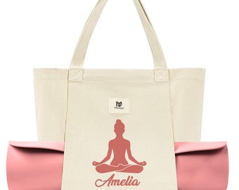 May include: A beige canvas tote bag with a pink yoga mat tucked inside. The bag has a pink silhouette of a woman in a yoga pose and the name "Amelia" printed on the front.