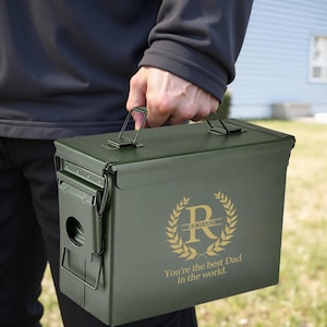May include: An olive green metal ammo box with a handle and latch. The box features a gold-colored design with the letter "R" and the name "Richard" inside a wreath, along with the text "You're the best Dad in the world."