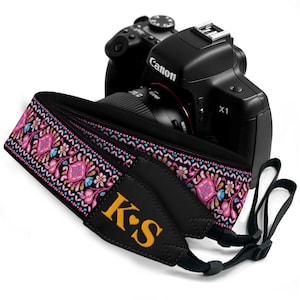 May include: A black Canon X1 camera with a patterned camera strap. The strap features a colorful floral design with pink, blue, and yellow accents. The strap has the initials "K❤️S" embroidered in yellow.