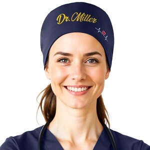 May include: A navy blue scrub hat with the text "Dr. Miller" embroidered in gold and a red heart with a white EKG line.