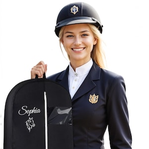 May include: A black equestrian helmet with a gold emblem, worn with a navy blue riding jacket and a white collared shirt. A black garment bag with the name "Sophia" embroidered on it and a horse head graphic is held in the image.