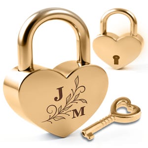 May include: Gold-colored heart-shaped padlocks with a matching key. One padlock has the initials "J" and "M" with a floral design. The key has a heart-shaped opening. The padlocks are a shiny gold color.