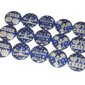 May include: Twelve blue and silver cheerleading buttons with different designs. Some buttons say "Cheer" with a silver pom-pom, some say "I'm a Cheerleader from Bow to Toe" with a silver cheerleader, and some say "To Cheer" with a silver heart.