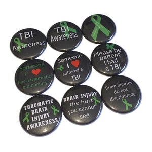 May include: Ten black and green button pins with white text and green ribbon designs. The pins promote awareness of traumatic brain injury (TBI). The text on the pins includes "TBI Awareness", "Someone has a traumatic brain injury", "Someone I love suffered a TBI", "Please be patient I had a TBI", "Brain injuries do not discriminate", "Brain Injury the hurt you cannot see", and "Traumatic Brain Injury Awareness".