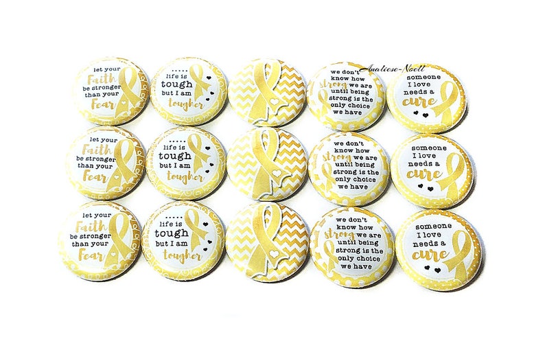 May include: Twelve 1-inch button pins with gold ribbon designs and inspirational messages. The messages include "Let your faith be stronger than your fear", "Life is tough but I am tougher", "We don't know how strong we are until being strong is the only choice we have", and "Someone I love needs a cure".