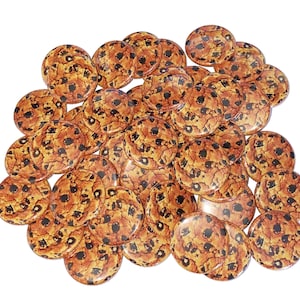 May include: A large group of round, brown and white cookie-shaped buttons. The buttons have a realistic image of chocolate chip cookies.