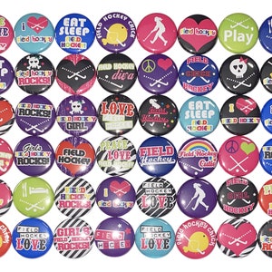 May include: A collection of 36 colorful round buttons with various field hockey-themed designs. The buttons feature text, graphics, and images related to field hockey, including the words "Field Hockey", "Love", "Peace", "Rocks", "Girl", "Cutie", and "Chic".