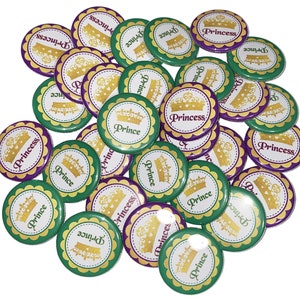 May include: A collection of round green and purple buttons with gold crowns and the words "Prince" and "Princess" printed on them.