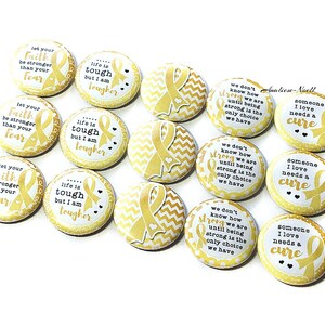 May include: A set of 10 yellow and white round buttons with gold ribbon designs and inspirational messages. The messages include "Let your faith be stronger than your fear", "Life is tough but I am tougher", and "We don't know how strong we are until being strong is the only choice we have".  The buttons also feature the message "Someone I love needs a cure".