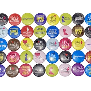 May include: A collection of colorful round buttons with various belly dancing themed phrases and designs. The buttons feature phrases like "Belly Dancer", "Shake It Up", "I Love Belly Dancing", and "Live Love Shimmy".