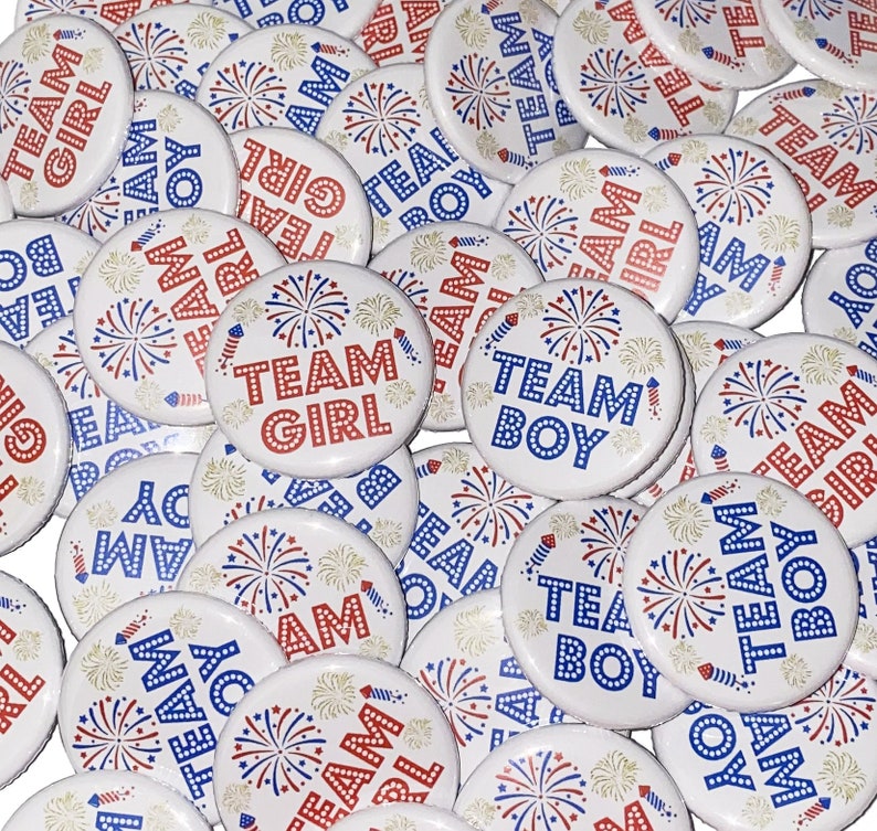 May include: A collection of round, white buttons with red, white, and blue firework designs. The buttons have the text "Team Girl" and "Team Boy" printed on them.