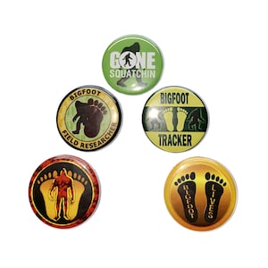 May include: Five round, colorful buttons with different Bigfoot designs. The buttons feature images of Bigfoot footprints, a Bigfoot silhouette, and the text "Bigfoot Field Researcher", "Bigfoot Tracker", "Gone Squatchin'" and "Bigfoot Lives".