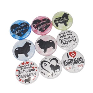 May include: A collection of nine round buttons with various designs featuring Australian Shepherds. The buttons have different backgrounds, including pink, blue, green, and white. Some buttons feature the text "Australian Shepherd" and "Love me, Love my Australian Shepherd".