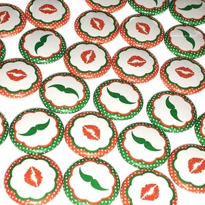 May include: A collection of round buttons with a white background, green and red polka dots, and a green mustache or red lips design.