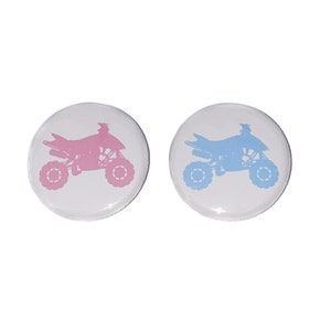May include: Two round buttons with white backgrounds and a silhouette of an ATV. One button has a pink ATV and the other has a blue ATV.