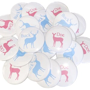 May include: A pile of white round buttons with blue and pink deer silhouettes. The buttons have the words "Buck" and "Doe" printed on them.