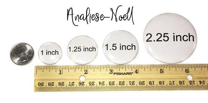 Op de afbeelding: Vier witte ronde knoppen in verschillende maten, met een diameter van 2,5 cm, 3,17 cm, 3,8 cm en 5,7 cm. De knoppen zijn van klein naar groot op een houten liniaal gelegd.
