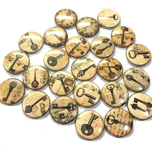 May include: A collection of 25 round, 1-inch diameter, key-themed buttons. Each button features a different vintage-style key design on a cream-colored background with black ink.