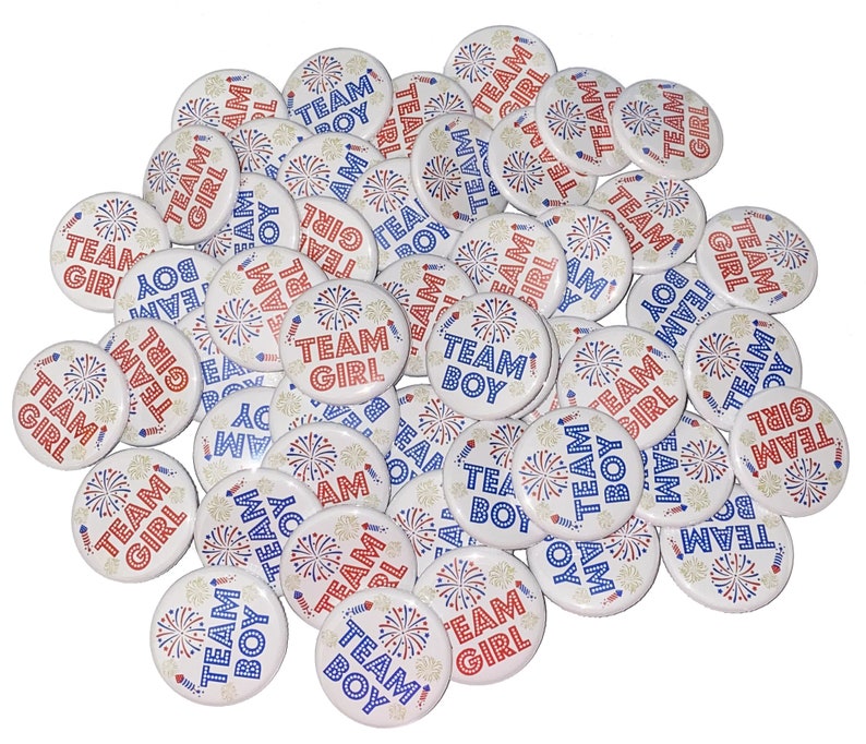 May include: A collection of round, white buttons with red and blue text and images. The buttons feature the words "Team Boy" and "Team Girl" with a firework design.