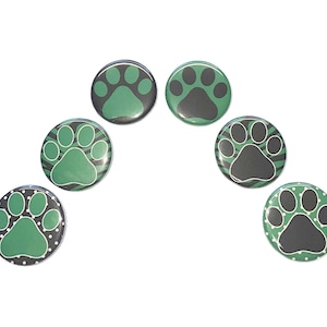 May include: Six round green and black paw print buttons. The paw prints are in a variety of patterns, including stripes, polka dots, and solid colors.