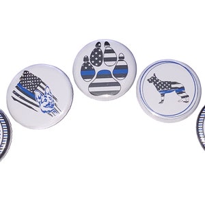 May include: Five round buttons with a thin blue line and American flag design. The buttons feature a paw print, a dog, and the word "LOVE" with a paw print and a gun.