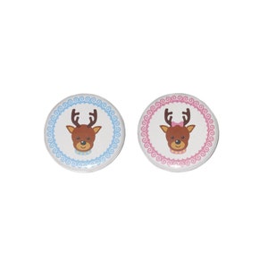 May include: Two round buttons with reindeer faces. The button on the left has a blue border and the button on the right has a pink border.
