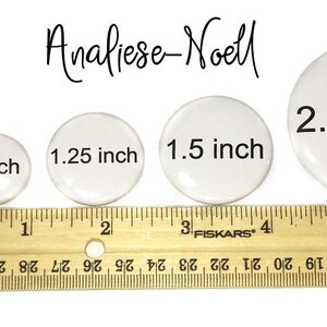 May include: Four white round buttons of different sizes, measuring 1 inch, 1.25 inches, 1.5 inches, and 2.25 inches. The buttons are lined up from smallest to largest on a wooden ruler.