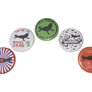 May include: Five round buttons with different designs featuring bearded dragons. The buttons have white backgrounds with black text and images. The text on the buttons reads "The beard makes the dragon", "Real dragons have beards", "Got crickets?", and "I raise tiny dinosaurs".