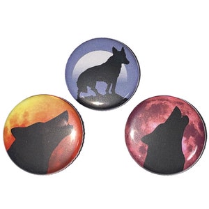 K&ouml;nnte beinhalten: Drei runde Kn&ouml;pfe mit Wolfssilhouetten vor einem Mondhintergrund. Der erste Knopf zeigt einen blauen Mond mit einem Wolf, der auf einem H&uuml;gel steht. Der zweite Knopf zeigt einen roten Mond mit einem Wolf, der zum Mond heult. Der dritte Knopf zeigt einen orangefarbenen Mond mit einem Wolf, der zum Mond heult.