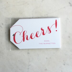 May include: White gift tag with red cursive text that says "Cheers!" and the text "XOXO, THE BURNETTES" in smaller red text.