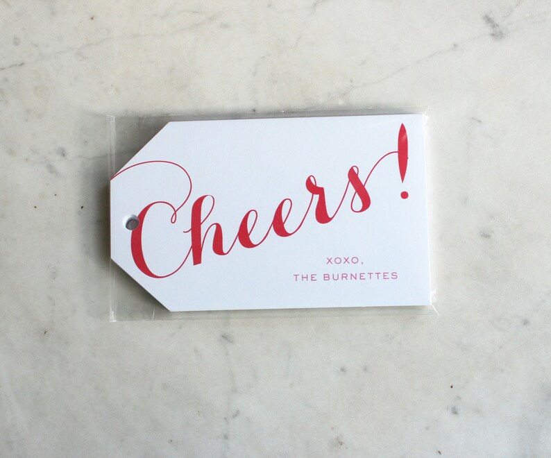 May include: White gift tag with red cursive text that says "Cheers!" and the text "XOXO, THE BURNETTES" in smaller red text.